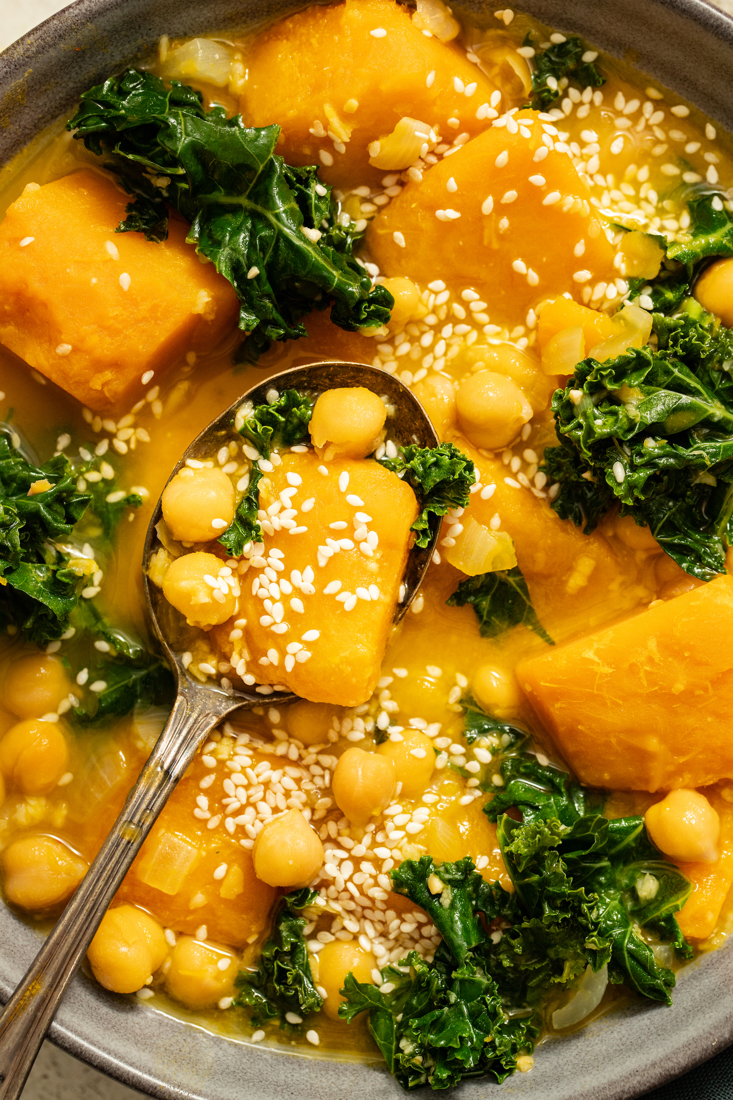Spoon resting in a bowl of our 1-Pot Kabocha Chickpea Miso Soup topped with sesame seeds