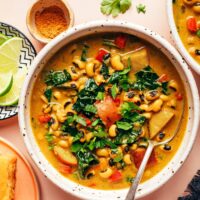 Overhead photo of a bowl of creamy curried black eyed pea soup next to ingredients used to make it and cornbread for serving
