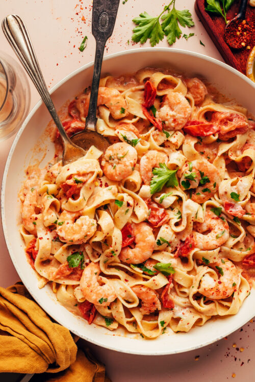 Serving spoons resting in a skillet of our dairy-free Tuscan shrimp pasta recipe