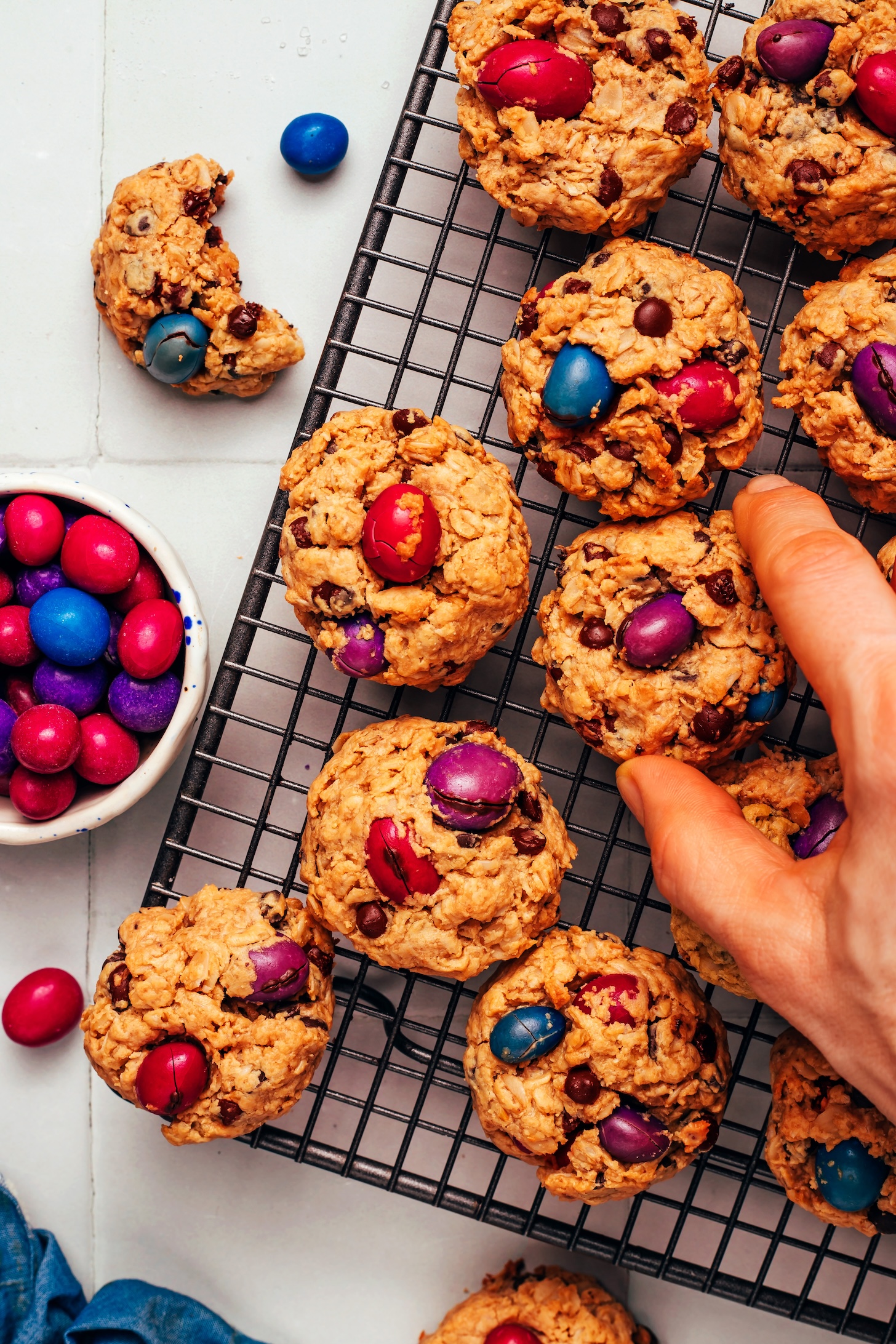Hand reaching for a monster cookie from a cooling rack