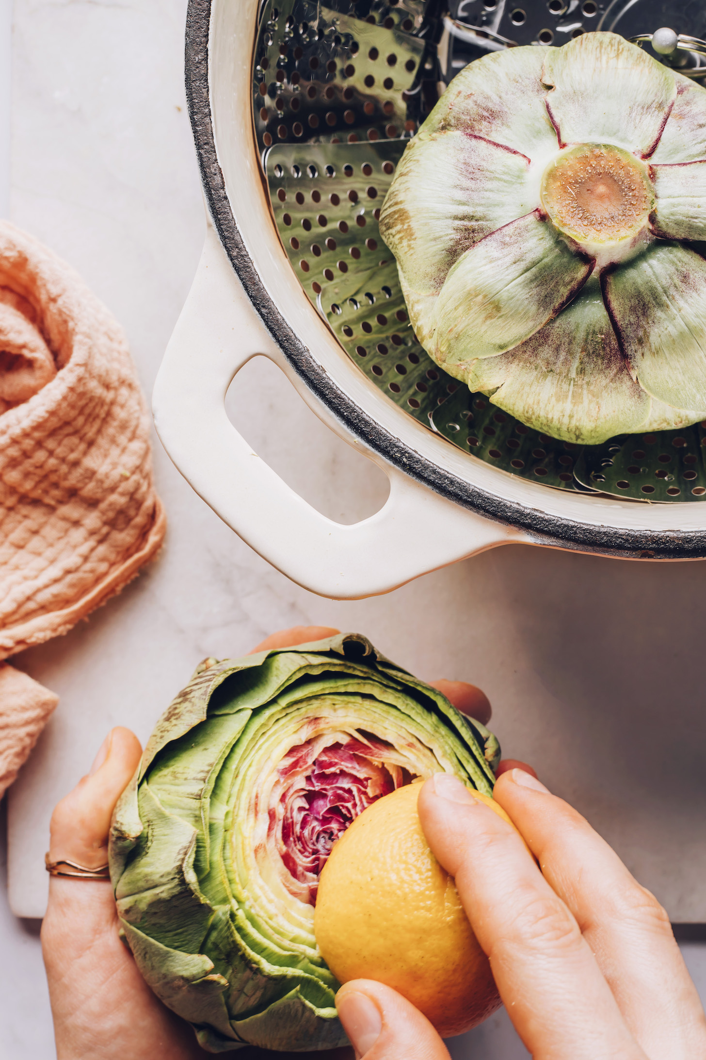Artichoke in a steamer basket and rubbing the other with lemon to prevent browning