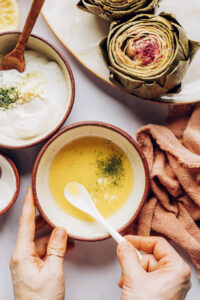 Steamed artichokes beside two bowls of sauces for dipping