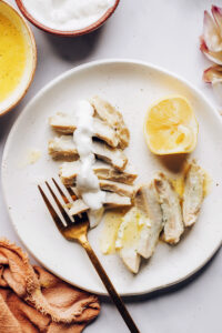 Artichoke hearts on a plate drizzled with lemon dill butter and lemon dill yogurt mayo dip