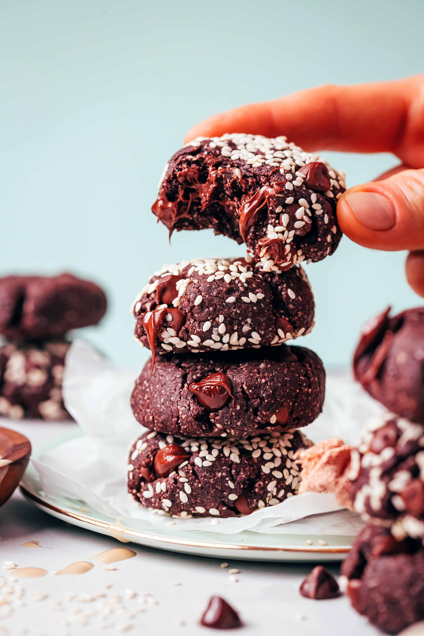 Holding a partially eaten double chocolate tahini cookie above a stack of more cookies