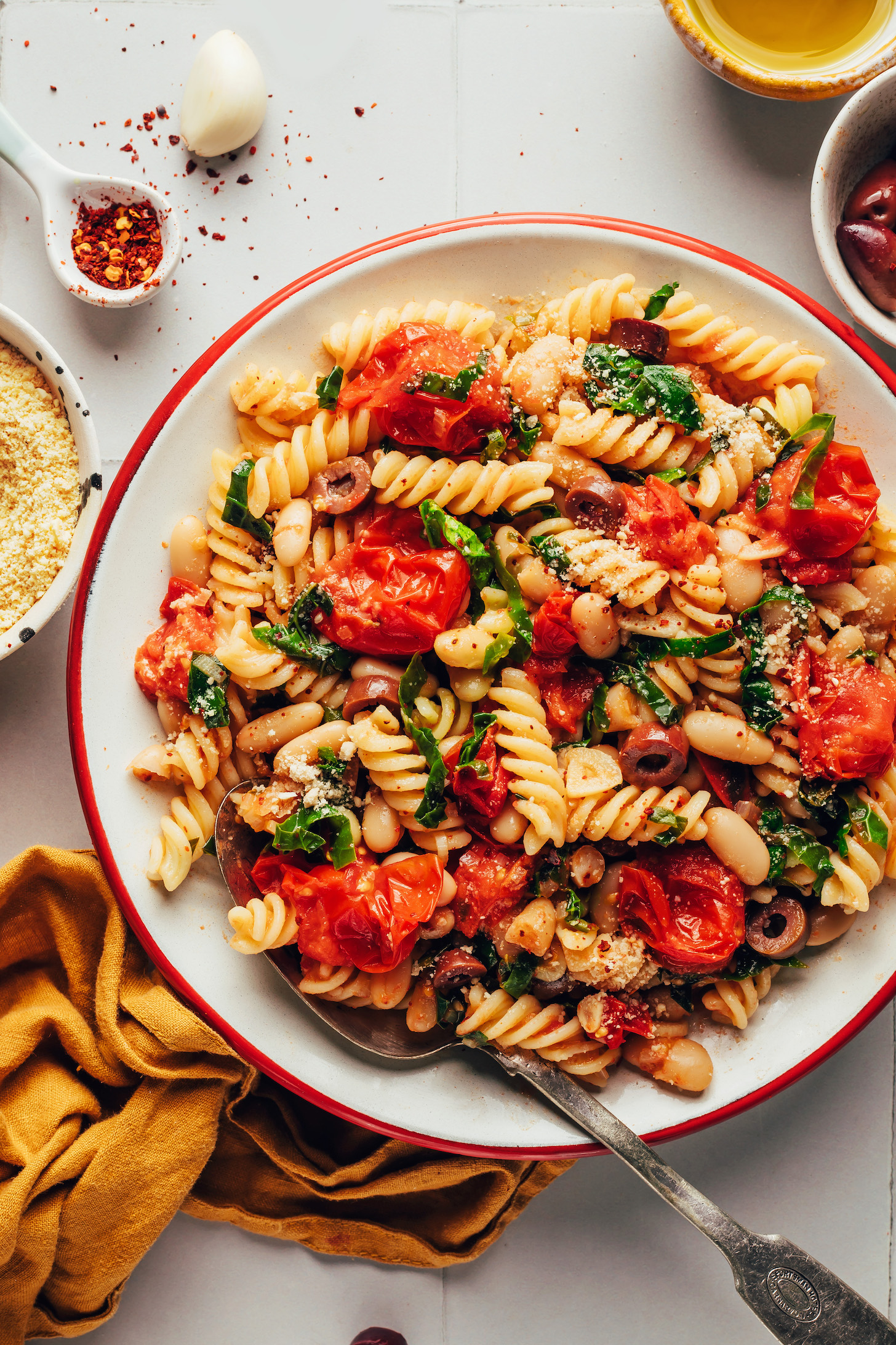 Large serving bowl of garlicky pasta with burst cherry tomatoes, kale, olives, and vegan parmesan cheese