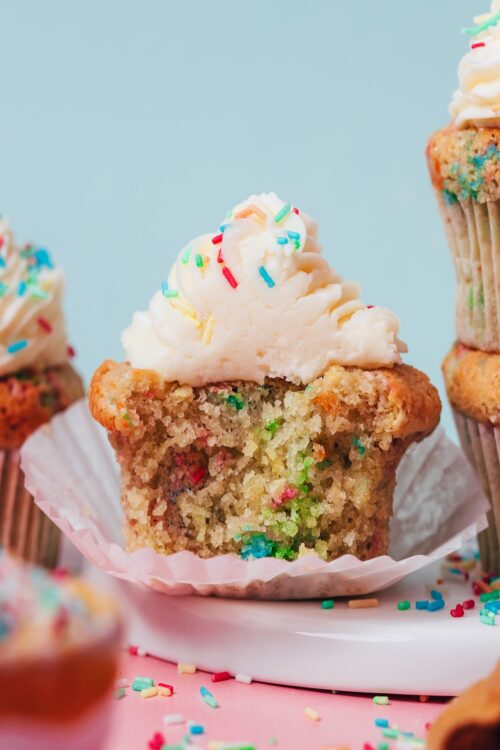 Partially eaten gluten-free funfetti cupcake topped with vanilla buttercream frosting