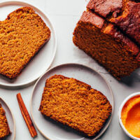 Slices of gluten-free pumpkin bread on a plate next to a partially sliced loaf