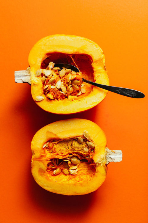 Halved pie pumpkin with a spoon scooping out the flesh and seeds to make Roasted Pumpkin Seeds