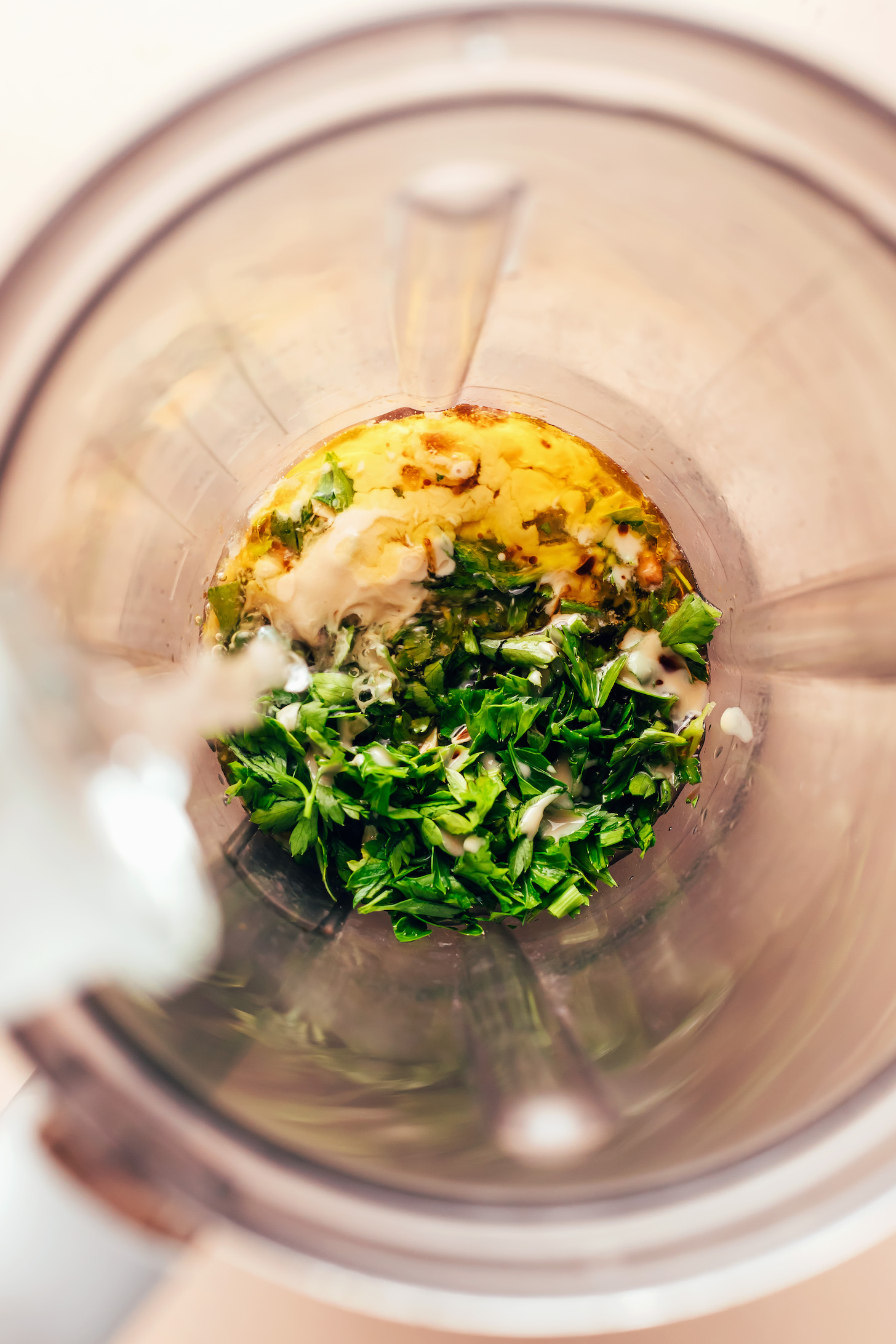 Pouring water into a blender to make a parsley tahini sauce