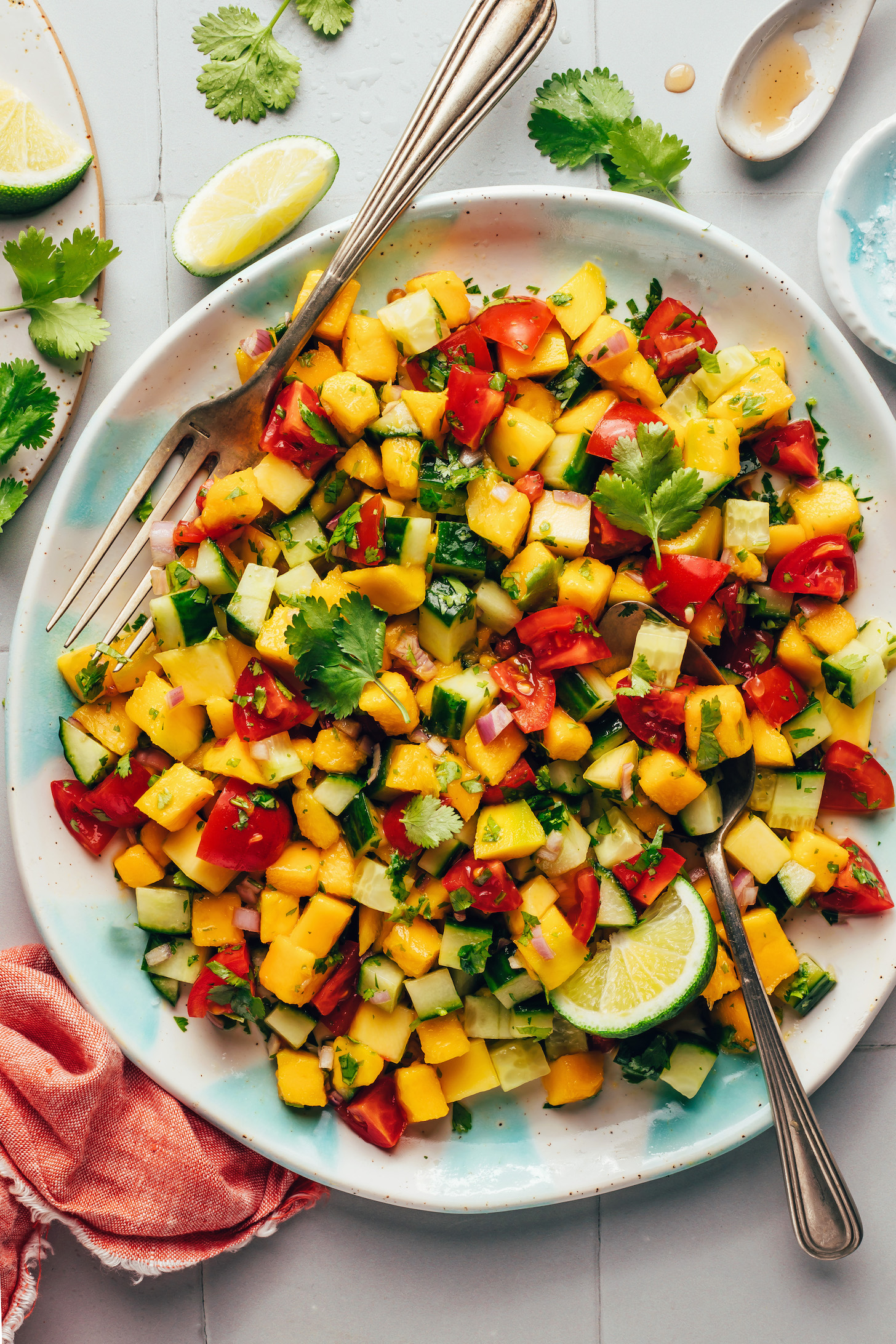 Spoon and fork in a bowl of mango cucumber salad