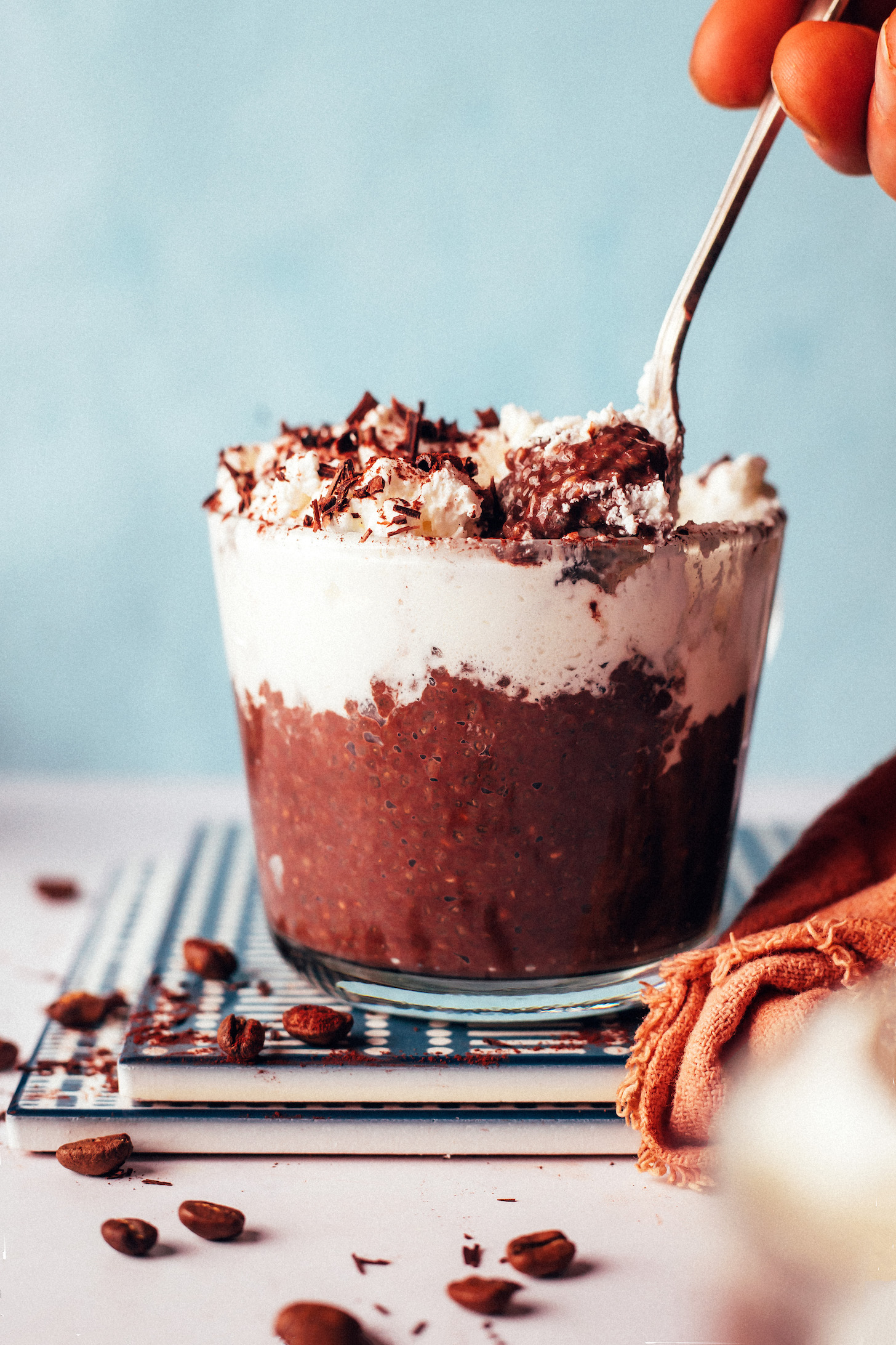 Spoon in a glass of mocha chia pudding topped with coconut whipped cream