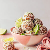 Bowl of coconut lime energy bites with lime wedges and shredded coconut scattered around