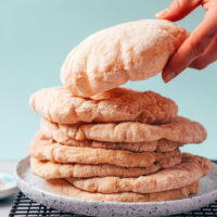 Hand picking up a piece of gluten-free pita from a stack with more pitas on a plate