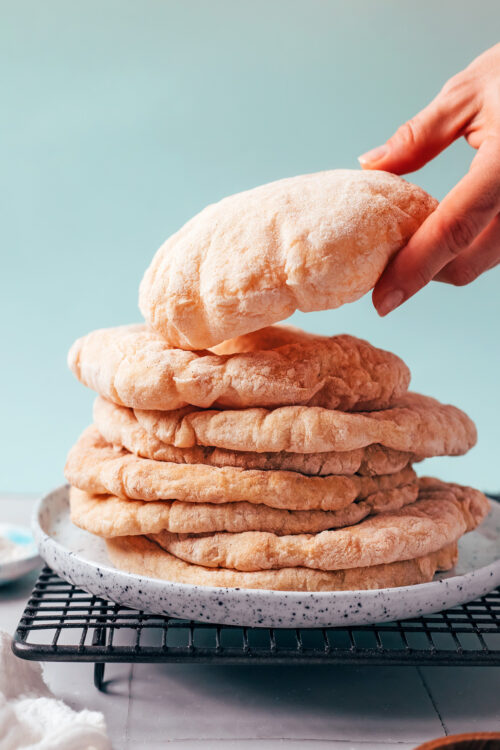 Hand picking up a piece of gluten-free pita from a stack with more pitas on a plate