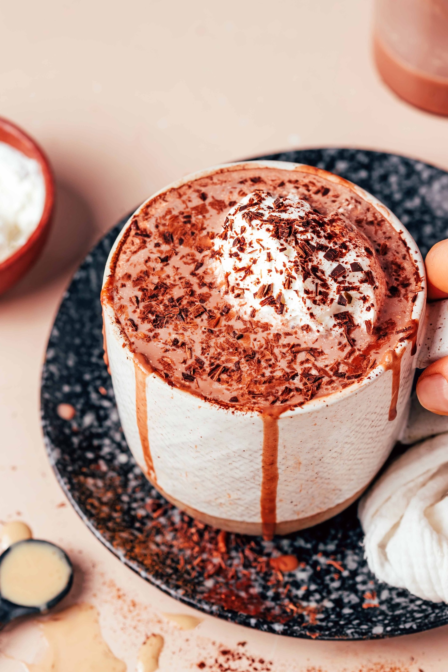 Holding the handle of an overflowing mug of tahini hot chocolate with whipped cream and chocolate