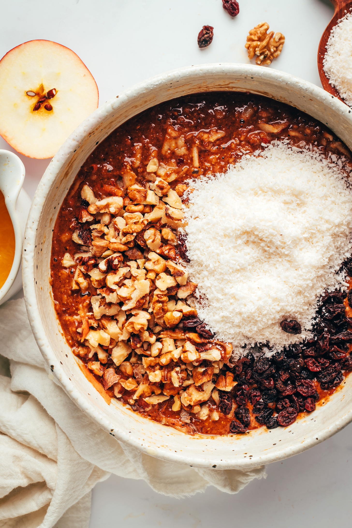 Bowl of muffin batter topped with walnuts, coconut, and raisins