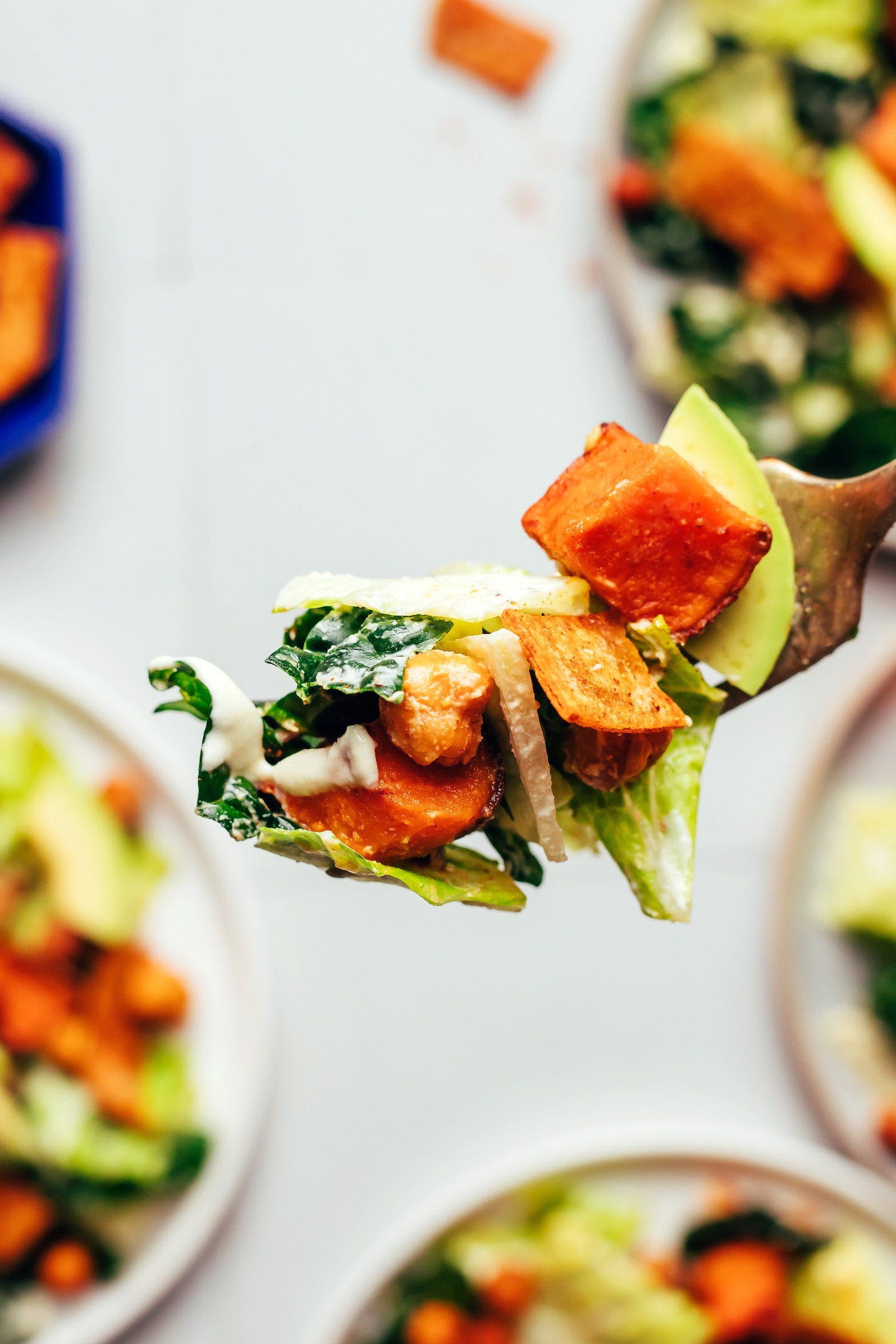 Fork with a bite of taco salad on it including avocado, romaine, kale, roasted chickpeas and sweet potato, dressing, and a tortilla strip