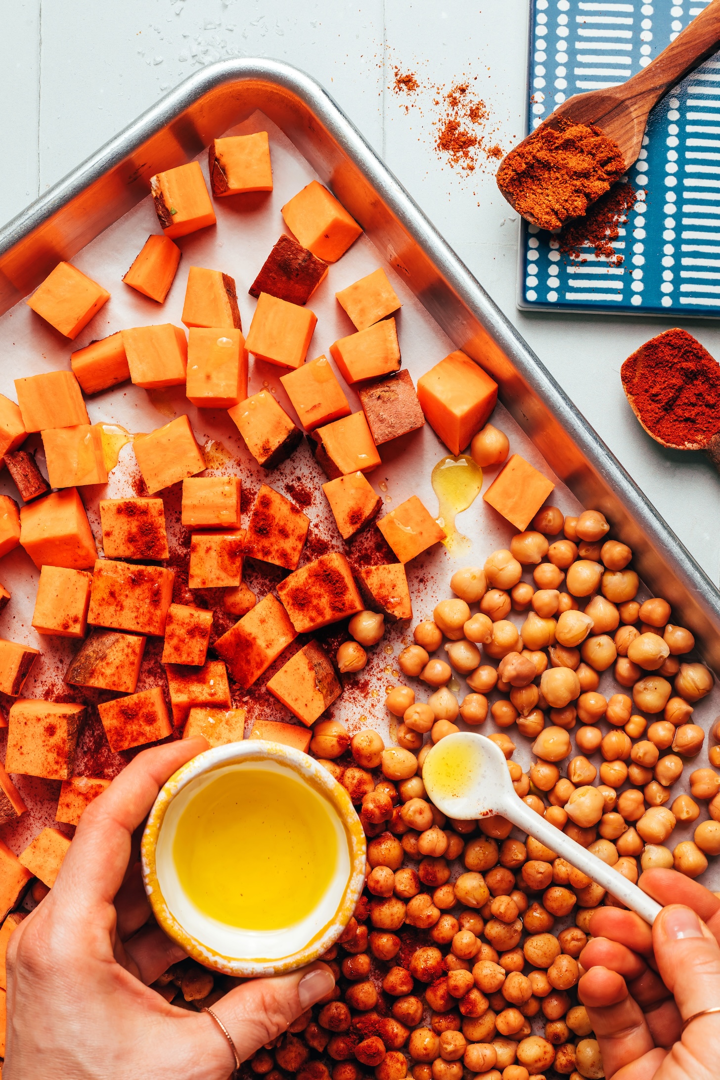 Adding oil onto a baking sheet of chickpeas and sweet potatoes